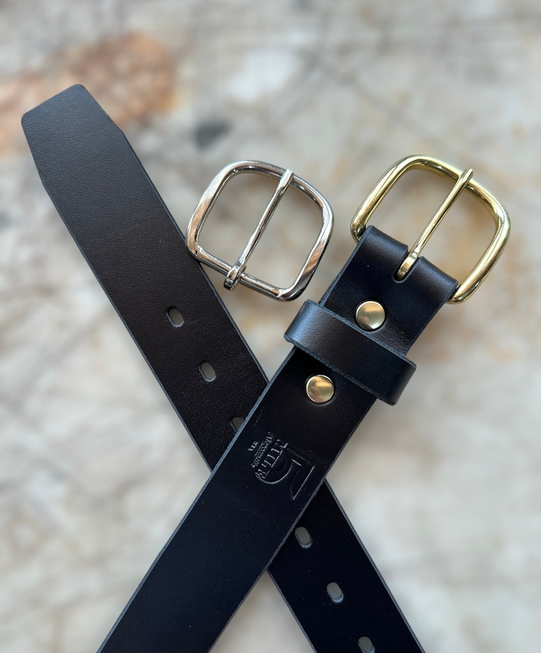 Black leather belt with gold and silver buckles on a textured surface