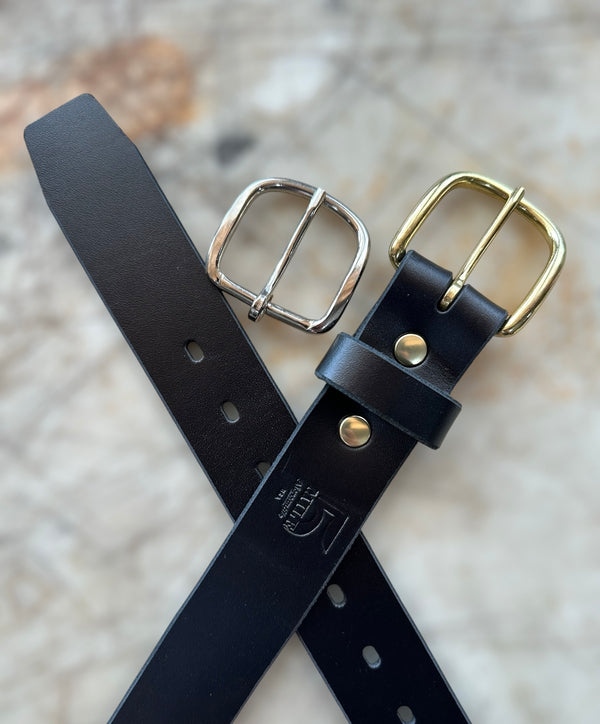 Black leather belt with gold and silver buckles on a textured surface