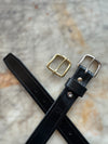 Black leather belt with gold and silver buckles on a textured surface