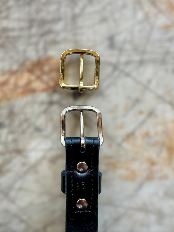 Two belt buckles, one gold and one silver, on a textured surface.