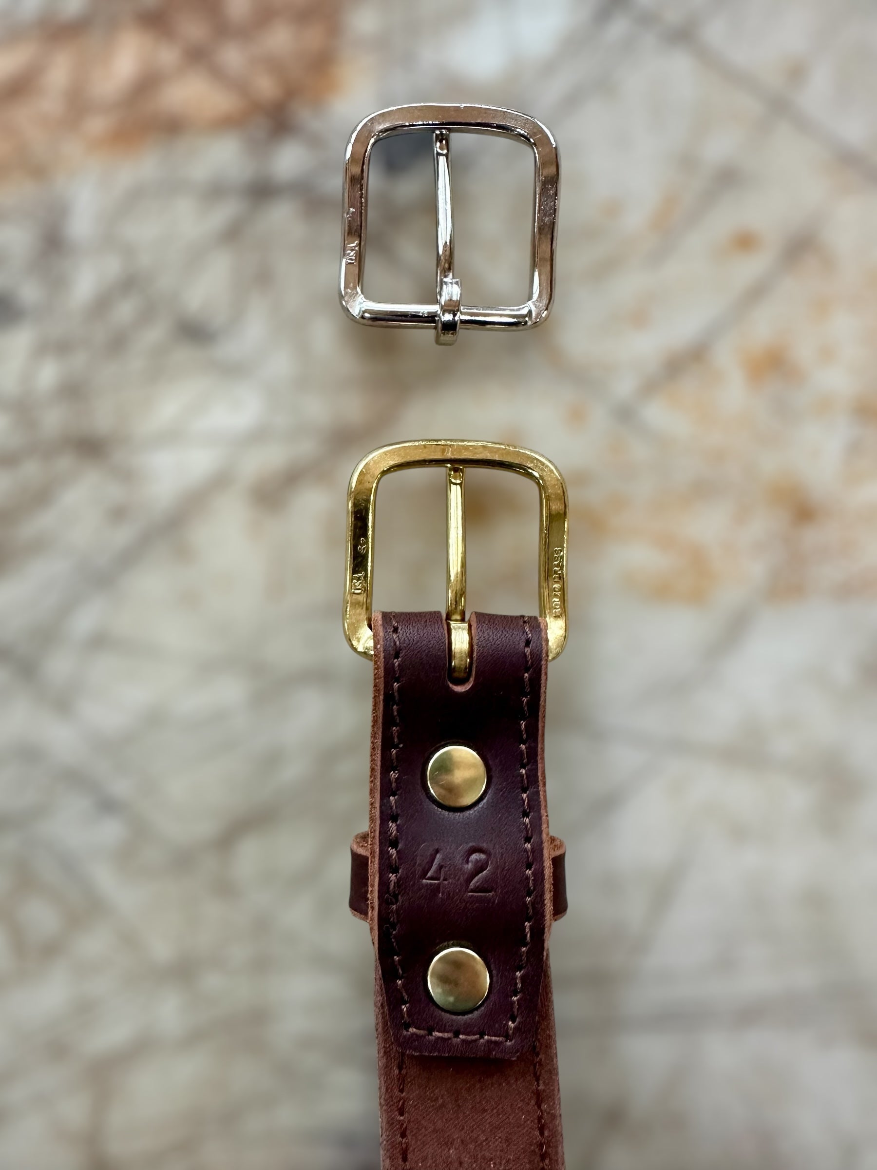 Gold and silver buckles with a brown leather strap on a textured surface