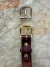 Gold and silver buckles with a brown leather strap on a textured surface