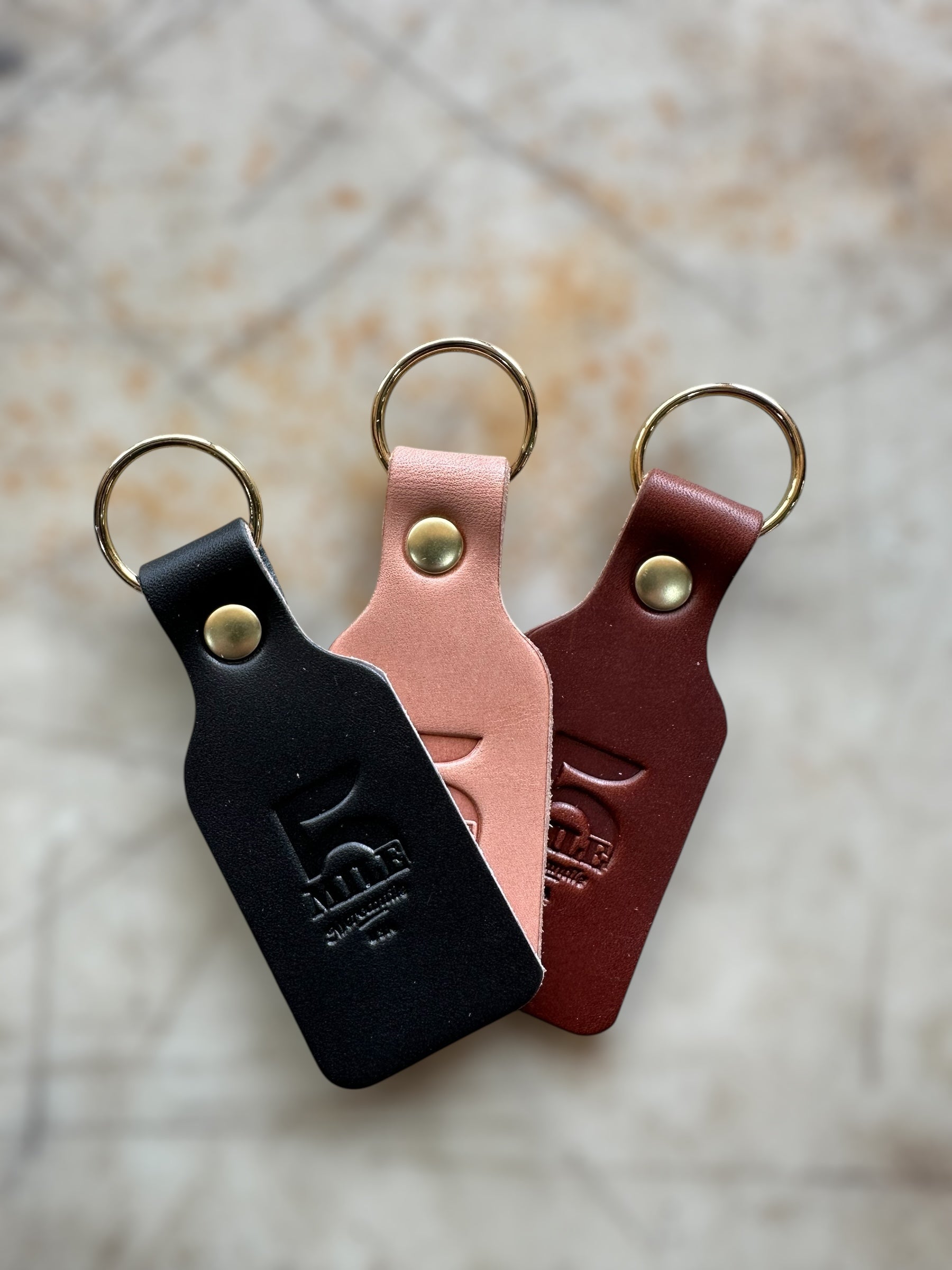 Three leather keychains in black, pink, and red on a textured surface.