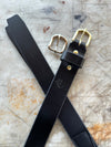 Black leather belt with brass buckles on a textured surface