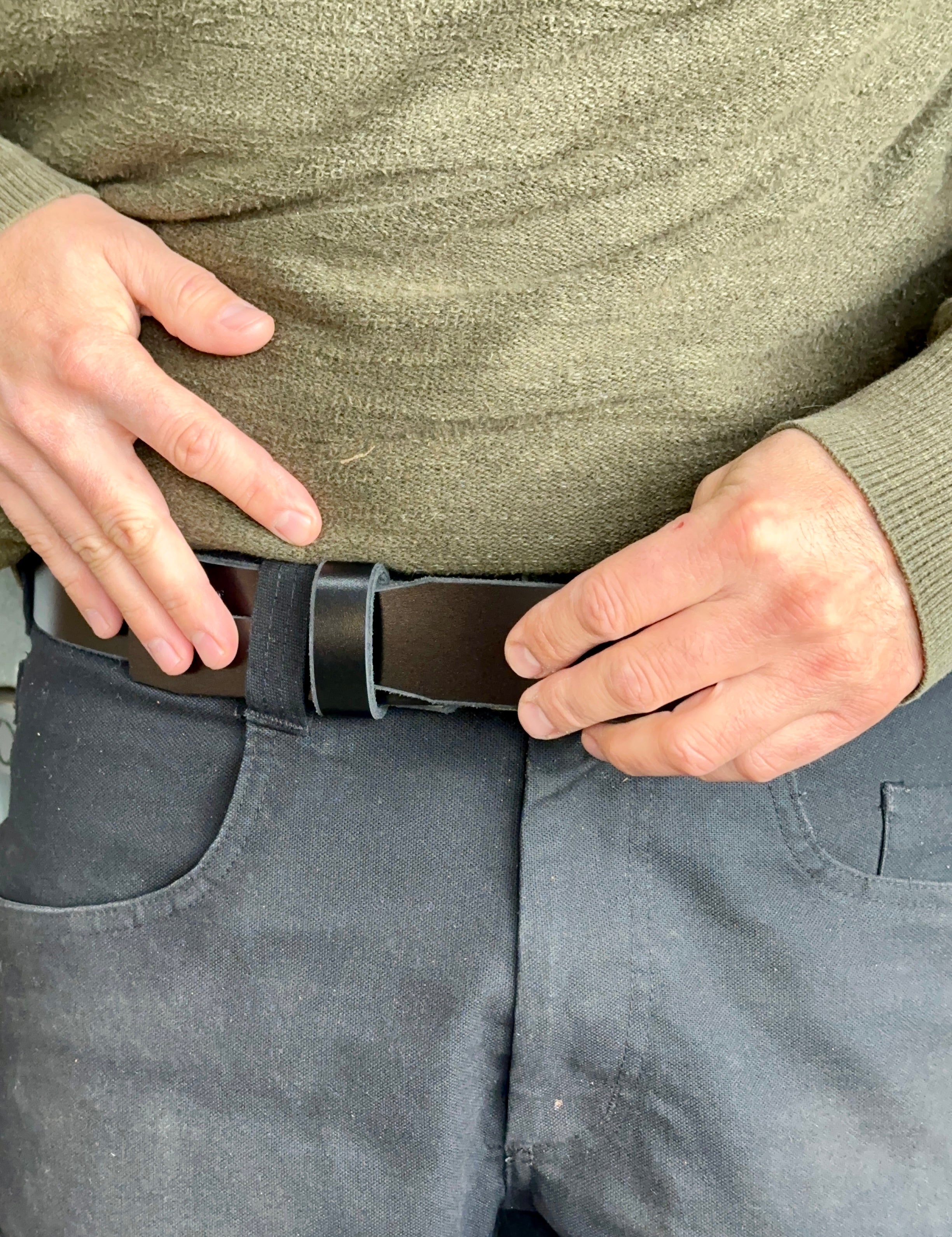Person adjusting a black belt on gray pants with a green sweater.