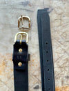 Black leather belt with brass and silver buckles on a textured surface