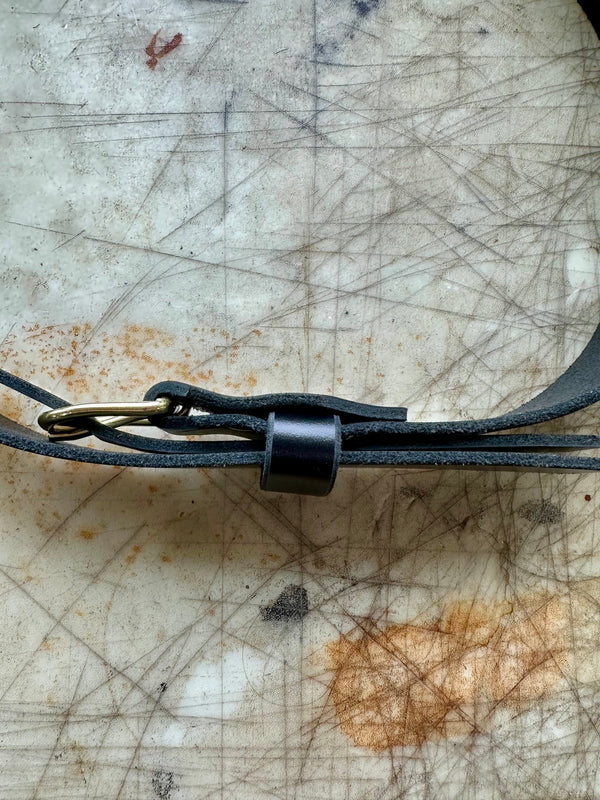 Close-up of a black leather belt with a brass buckle on a textured surface