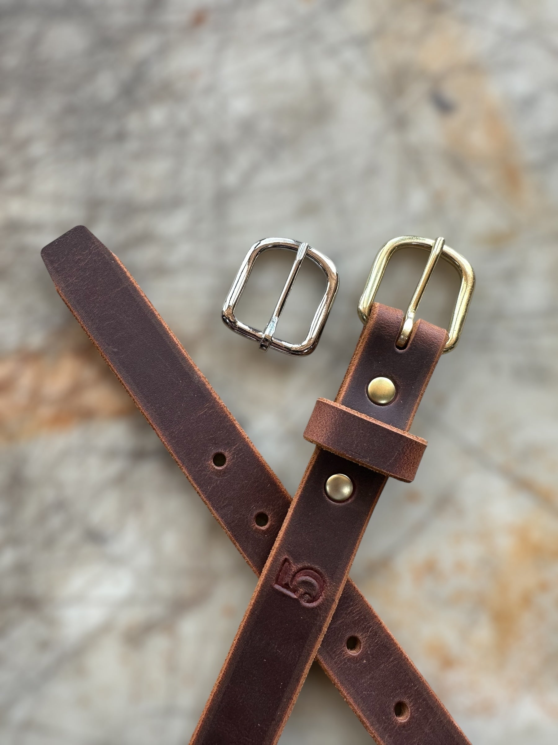 Brown leather belt with two buckles on a textured surface