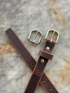 Brown leather belt with two buckles on a textured surface