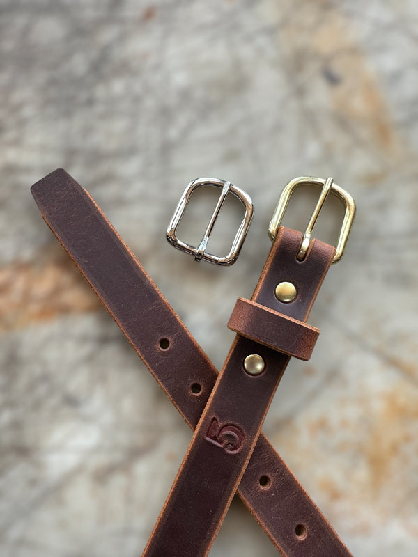Brown leather belt with two buckles on a textured surface