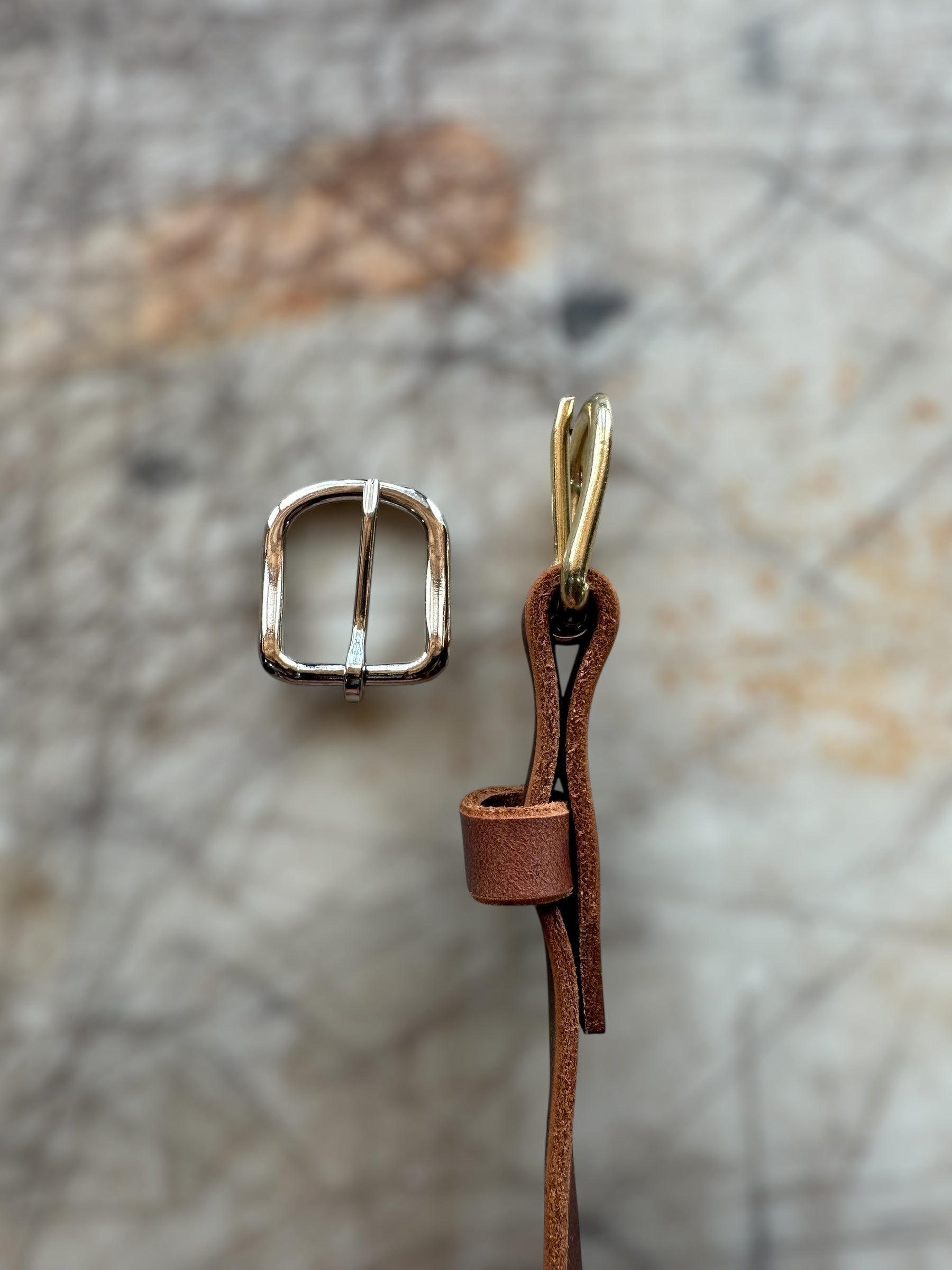Gold buckle and brown leather strap on a textured stone background