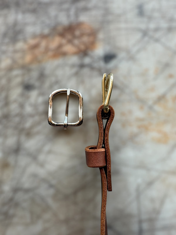 Gold buckle and brown leather strap on a textured stone background