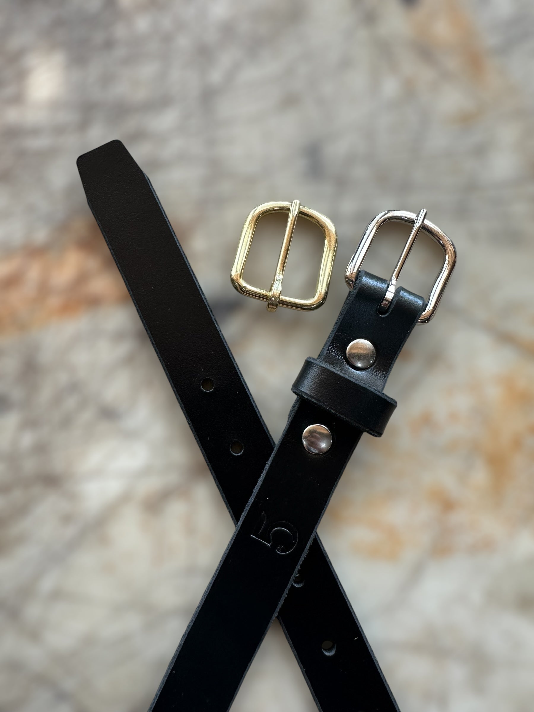 Black leather belt with gold and silver buckles on a textured surface