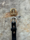 Gold and silver belt buckles on a black leather strap against a textured background