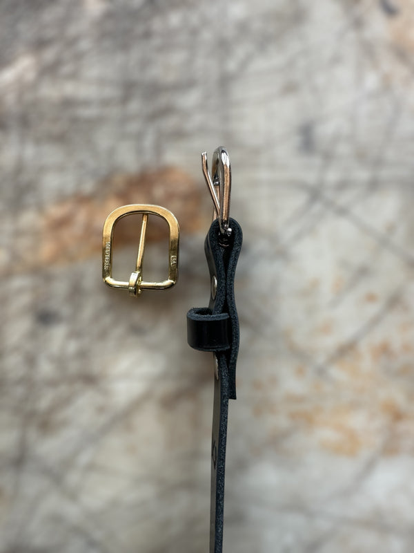 Gold buckle and black leather strap on a textured stone background