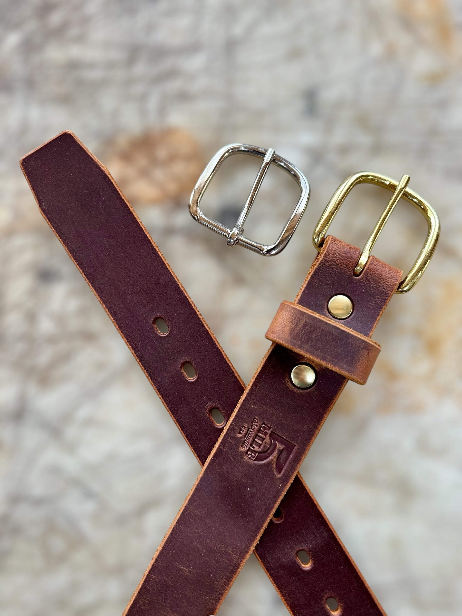 Brown leather belt with gold and silver buckles on a textured surface
