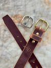 Brown leather belt with gold and silver buckles on a textured surface