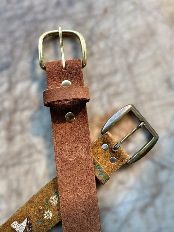 Two brown leather belts collars with brass buckles on a textured surface.