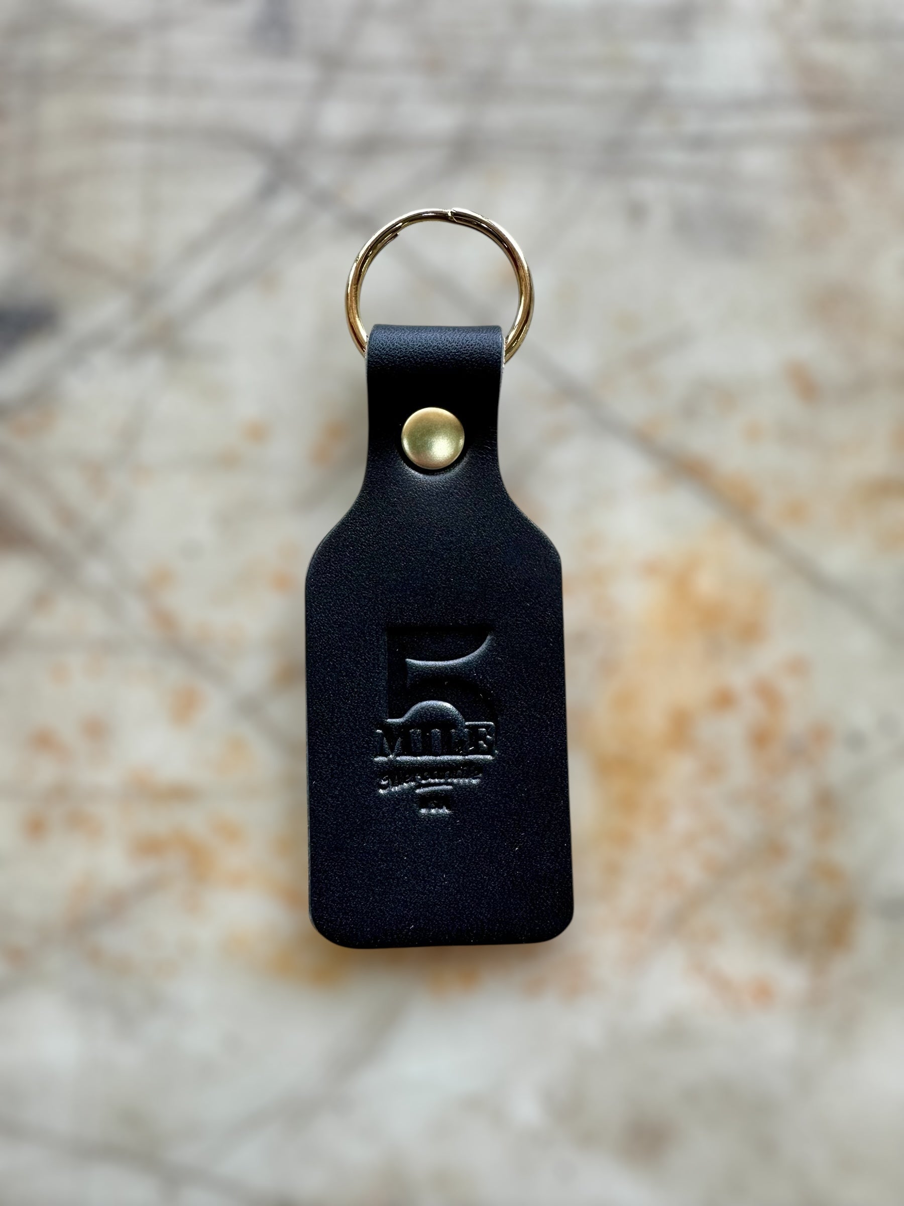 Black leather keychain with gold ring and metal clasp on a textured surface