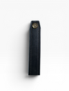 A close-up of a black leather strap or sleeve with visible stitching and a brass snap button, shown against a plain white background.