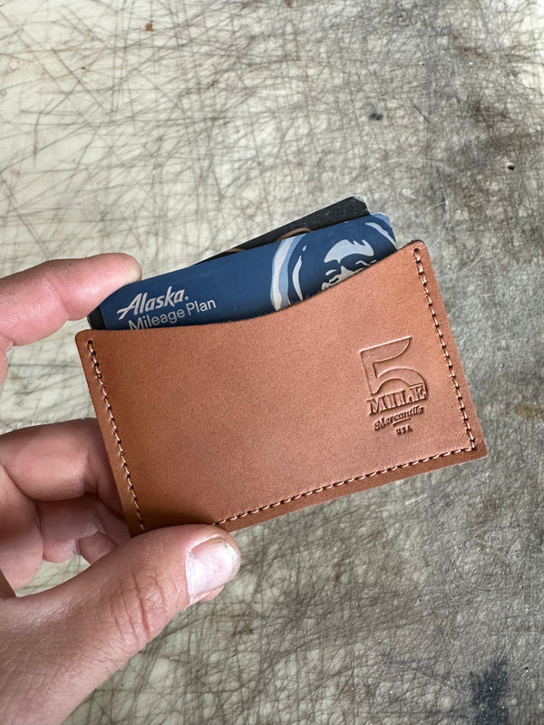 Brown leather wallet with card holder held by a hand on a textured surface
