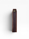 A close-up of a dark brown leather strap or belt section with visible stitching and a small brass-tone metal rivet near the top, shown against a plain white background.