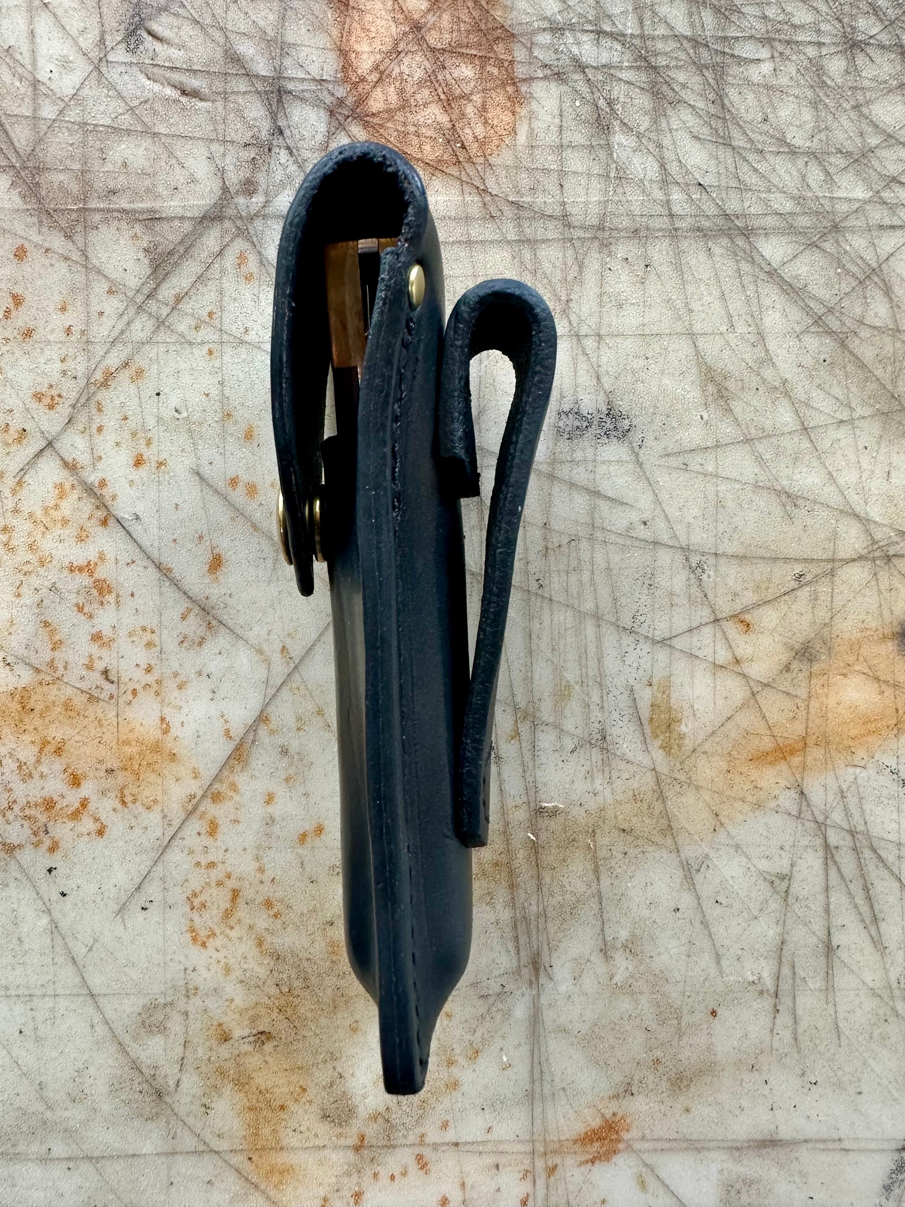 Black leather knife sheath with brass fasteners on a textured surface side profile