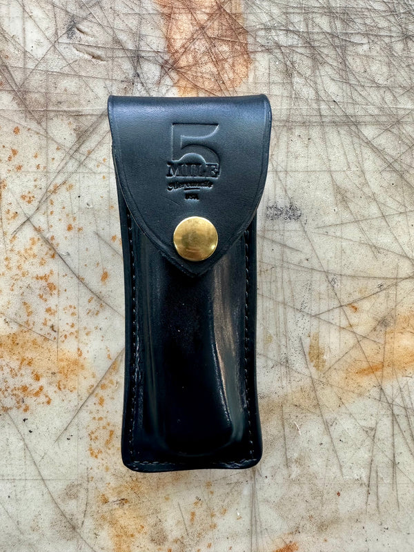 Black leather tool pouch with brass snap on a textured surface