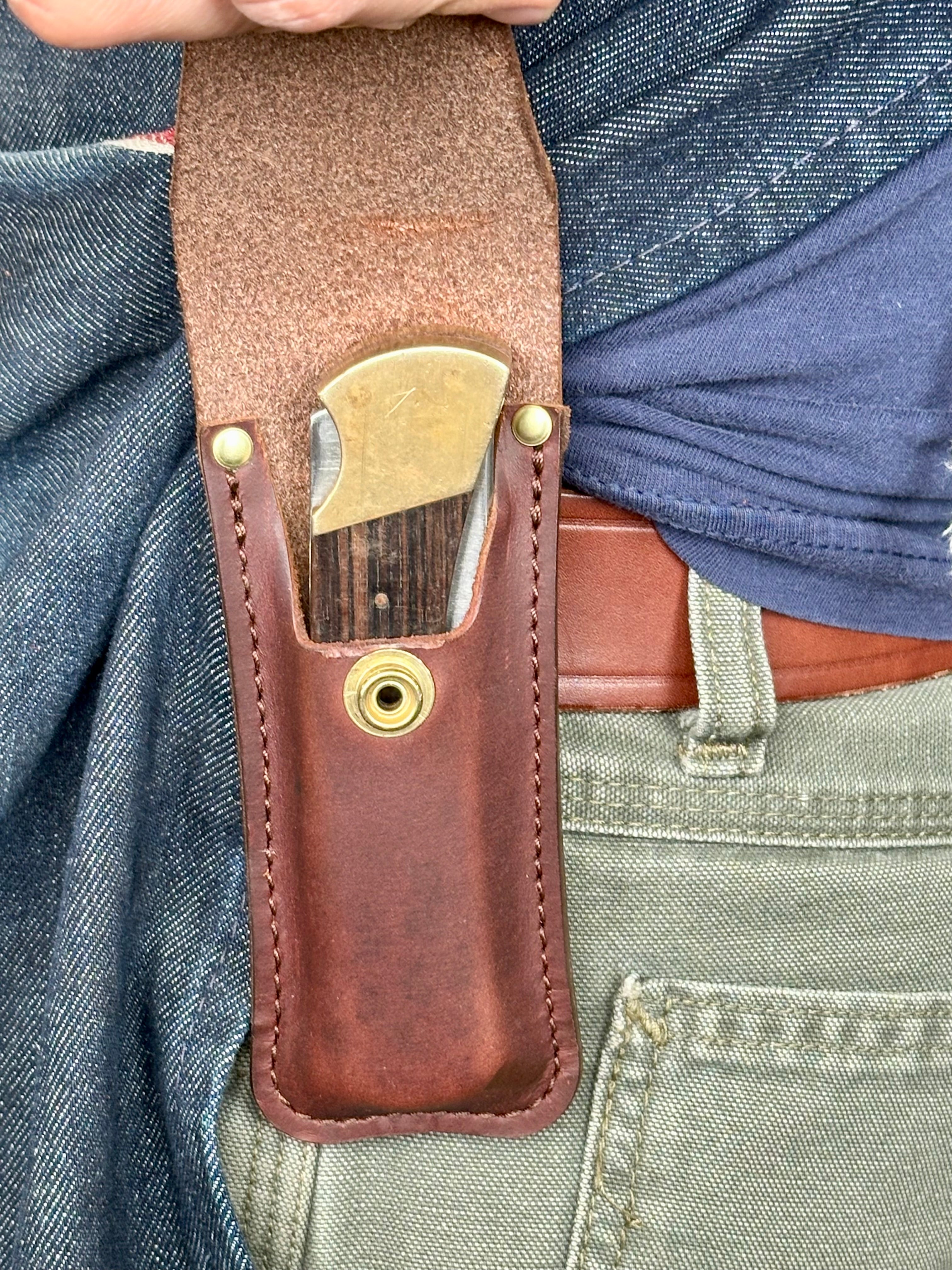Brown leather knife sheath with brass fasteners worn on a person's waist.