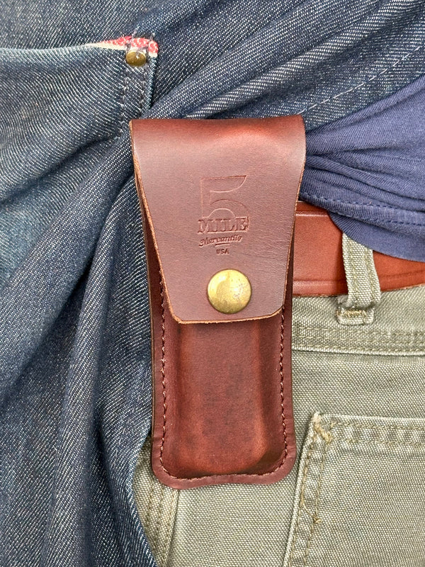 Brown leather pouch with a visible brand logo attached to a person's waistband.