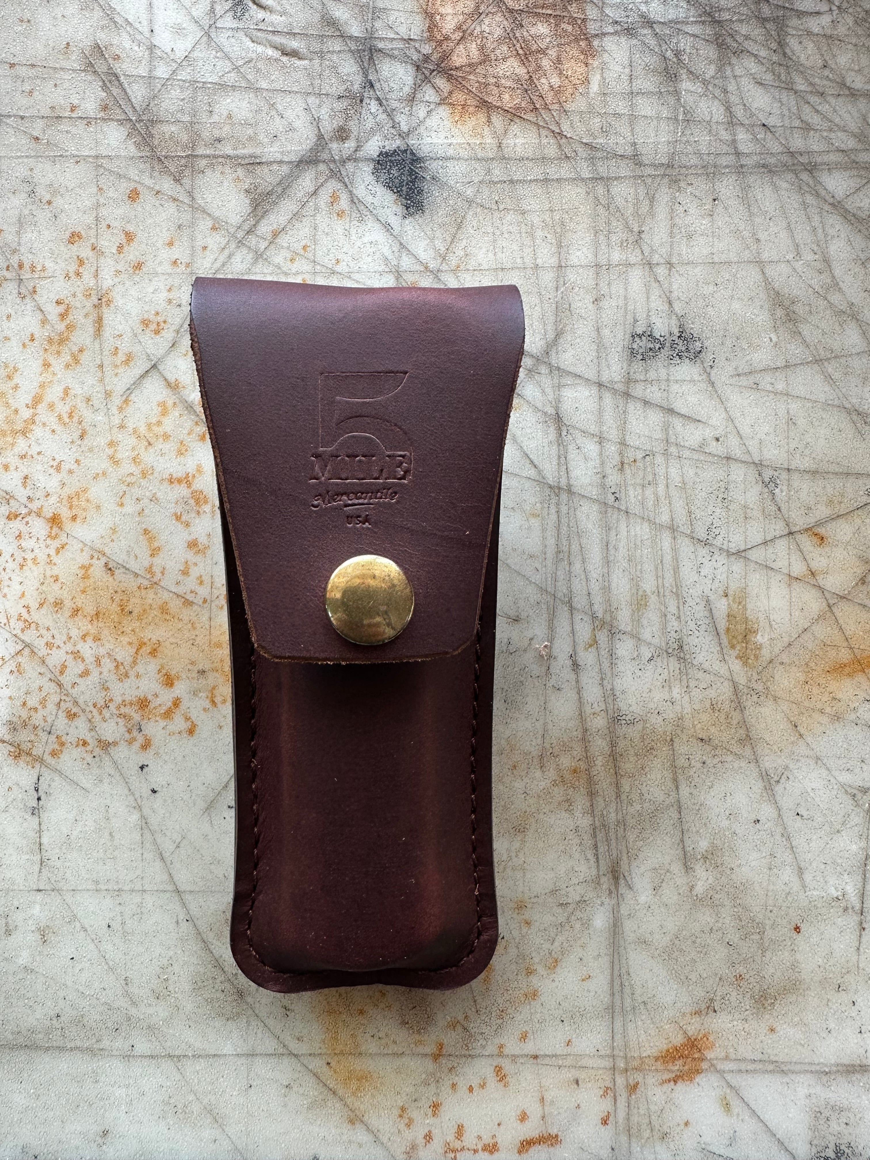 Brown leather pouch with brass button on a textured surface