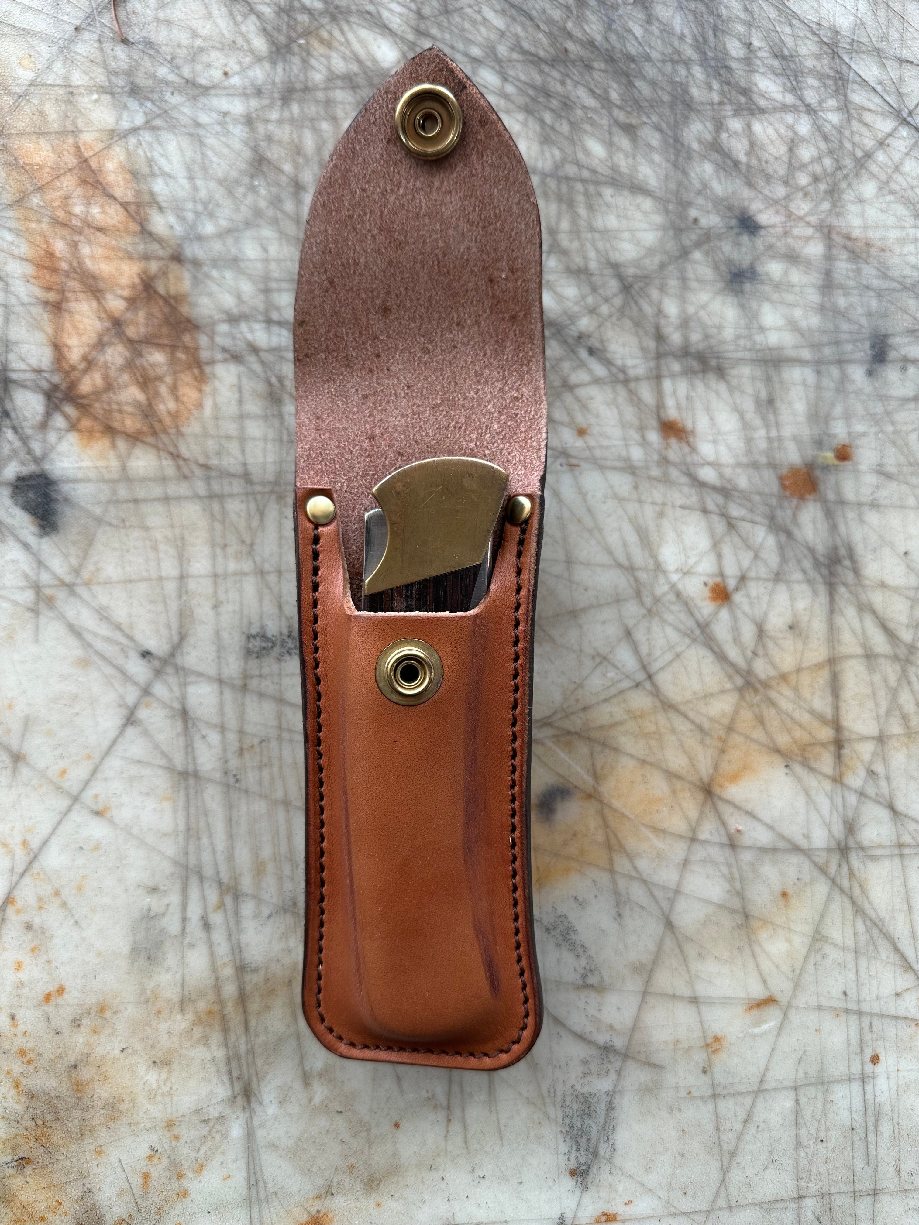 Brown leather knife sheath with metal clip on a textured surface