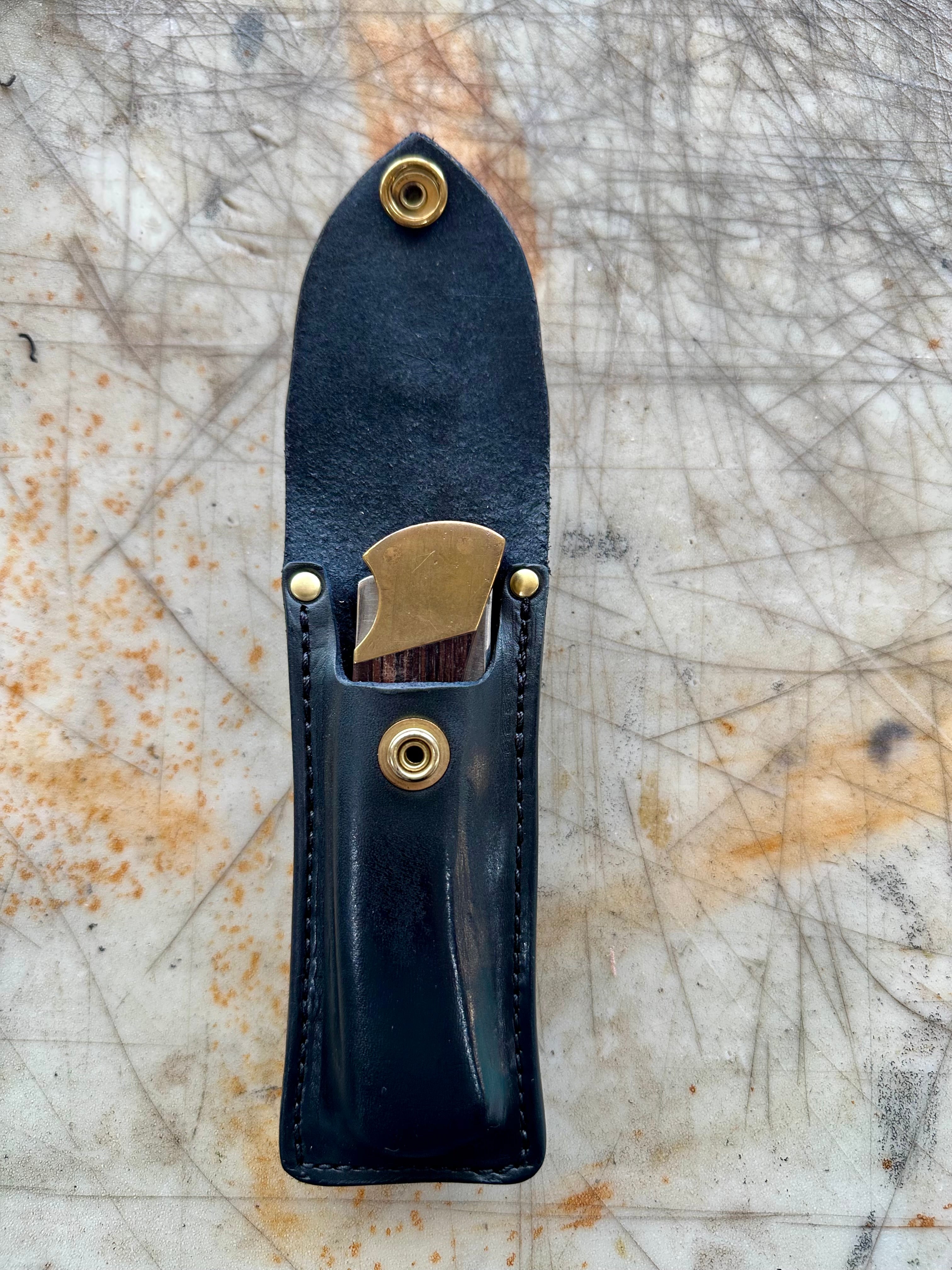 Black leather knife sheath with brass fasteners on a textured surface
