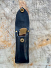 Black leather knife sheath with brass fasteners on a textured surface