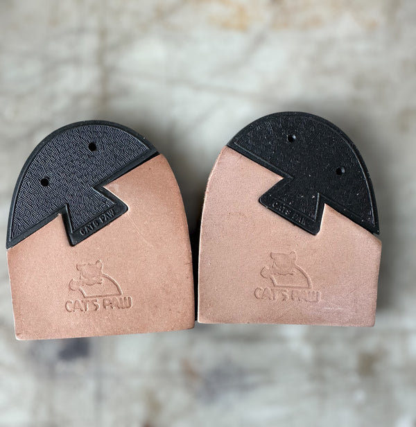 A pair of Cat's Paw heel caps for shoes, featuring a natural tan leather lower section with an embossed cat logo and brand name, and a black textured upper section.