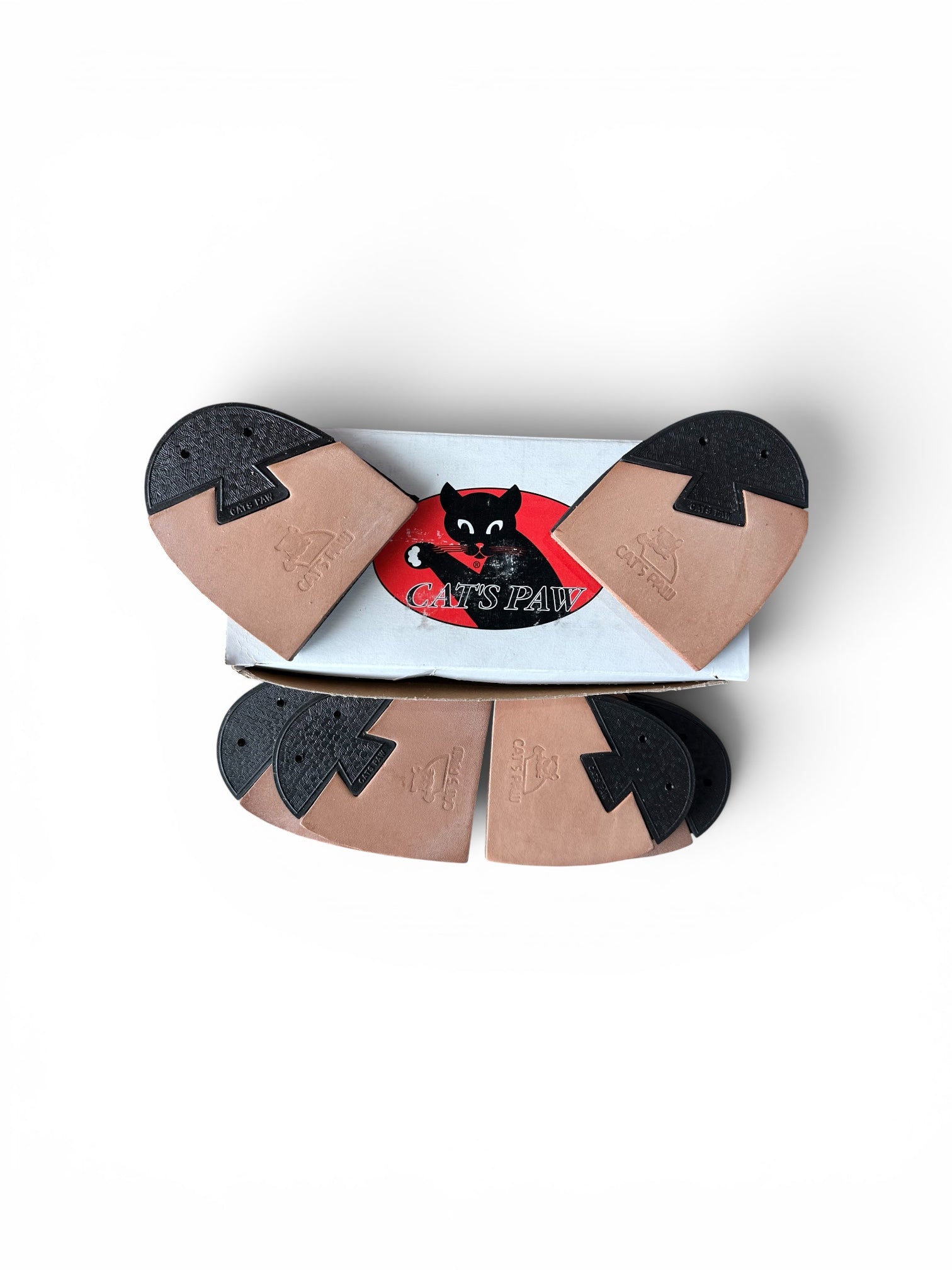 A pair of tan and black rubber shoe soles arranged in a fan shape above their white and red cardboard packaging, featuring a black cat logo and the brand name 'CATS PAN'.