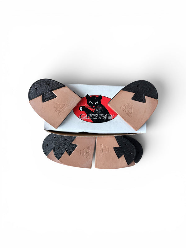 A pair of tan and black rubber shoe soles arranged in a fan shape above their white and red cardboard packaging, featuring a black cat logo and the brand name 'CATS PAN'.