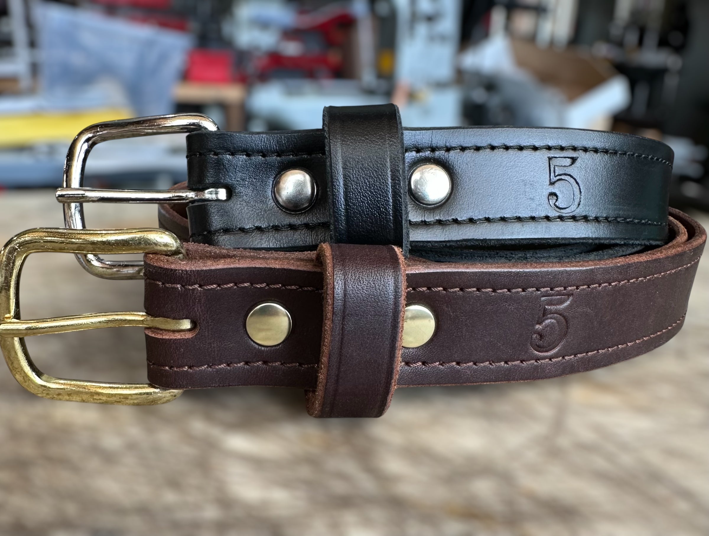 Two leather belts with brass and silver buckles on a blurred background