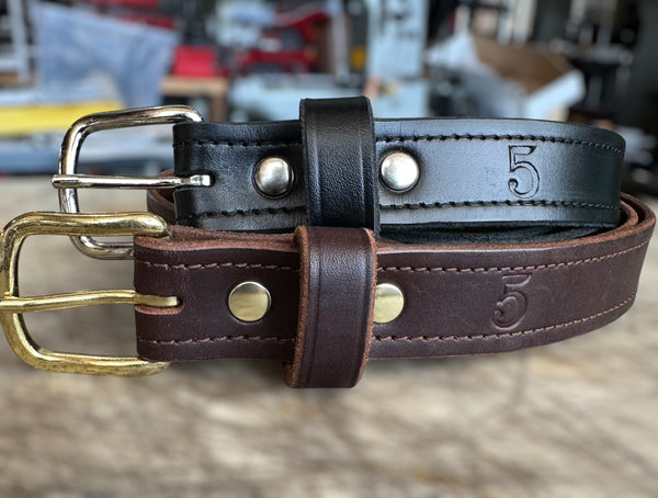 Two leather belts with brass and silver buckles on a blurred background