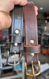 Two leather belts with metal buckles held by a hand in an indoor setting.