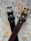 Two leather belts with brass and silver buckles on a textured surface