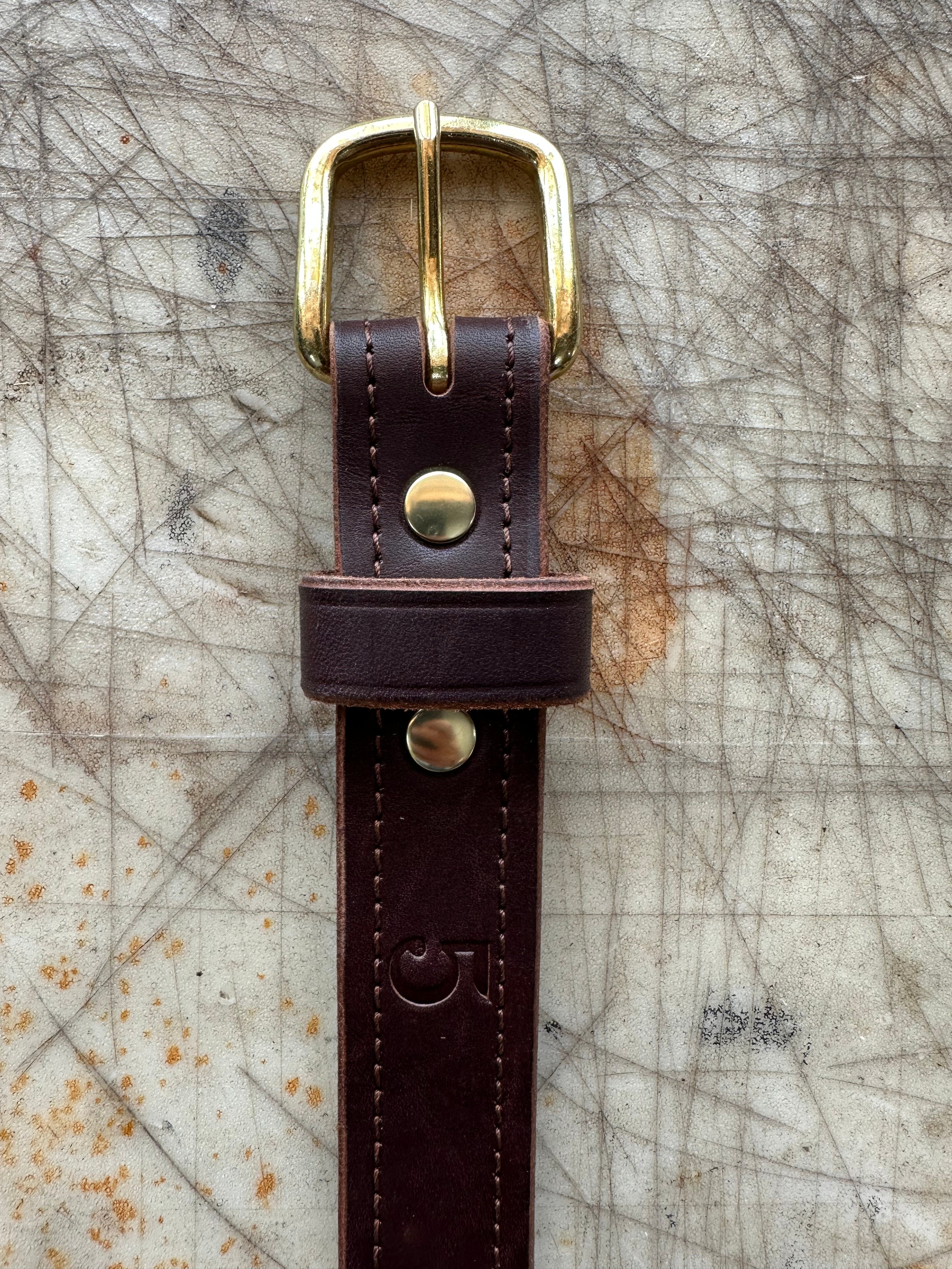Brown leather belt with brass buckle on a textured surface