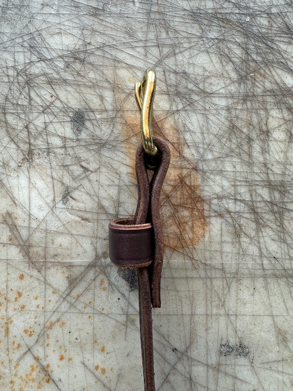 Brown leather strap with brass hook on a textured surface