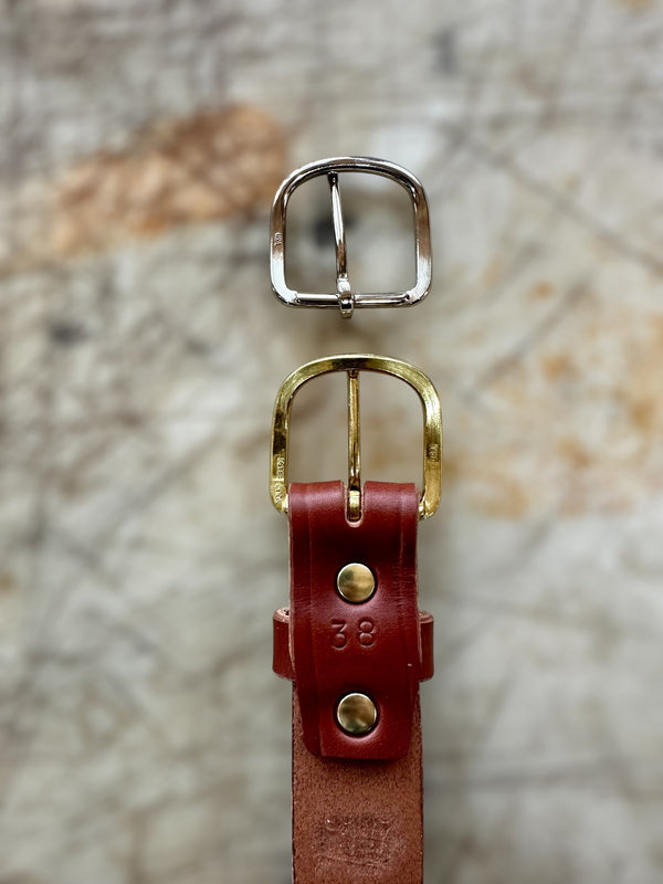 Two belt buckles, one gold and one silver, on a textured stone surface.