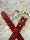 Red leather belt with gold and silver buckles on a textured surface