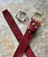 Two red leather straps with metal buckles on a textured surface