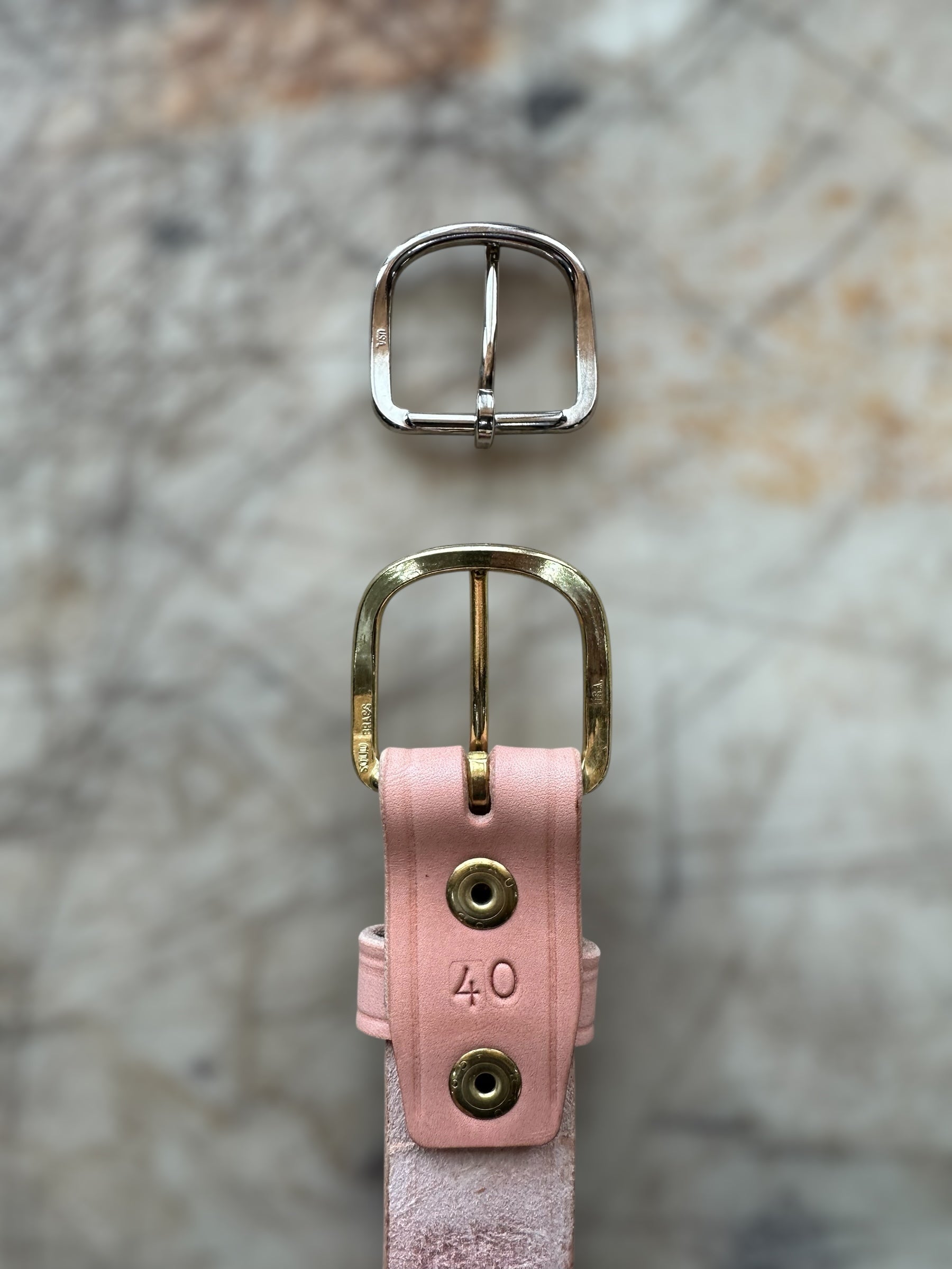 Pink leather belt with gold buckle and silver metal buckle on a textured surface