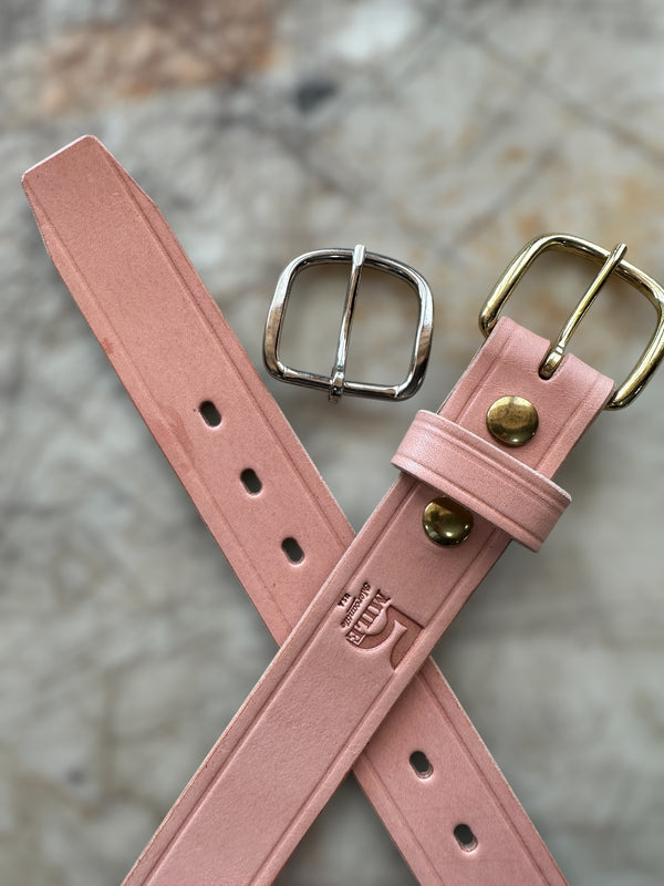 Pink leather belt with two buckles on a textured surface