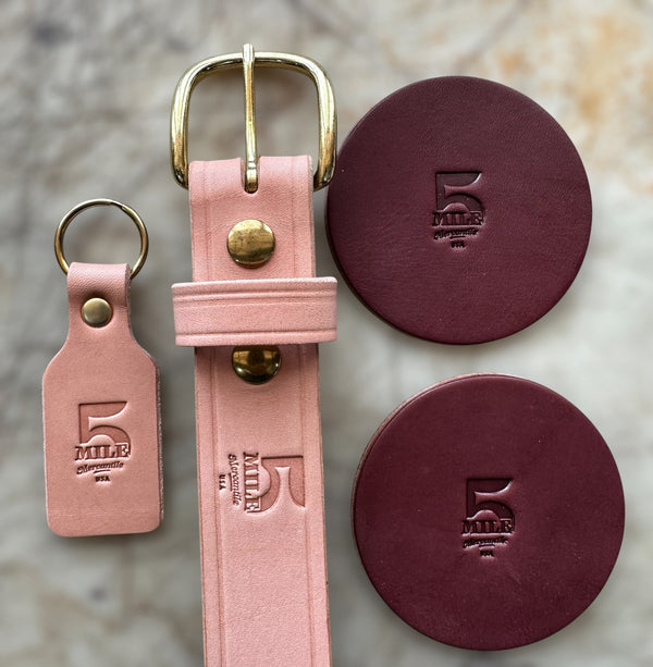 Pink leather belt with gold buckle and matching keychain on a textured surface.