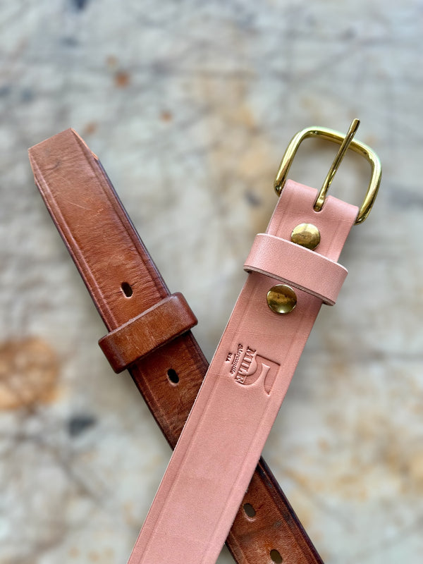 Two leather straps, one brown and one pink with a gold buckle, on a textured surface.